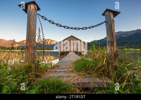 Kette vor dem Weg zu einem hölzernen Bootshaus am Ufer des Kochelsees vor Herzogstand und Jochberg in der Abendsonne im Herbst Stockfoto