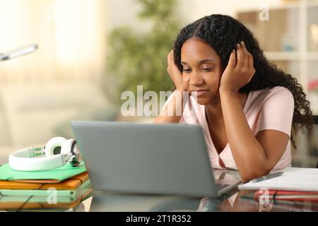 Enttäuschte schwarze Studentin, die zu Hause den Laptop überprüft hat Stockfoto