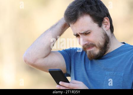 Trauriger Mann, der auf dem Smartphone schlechte Inhalte im Freien überprüft Stockfoto