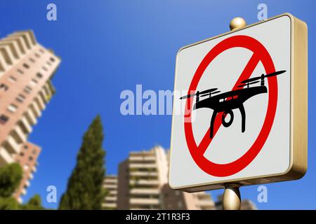 Drohnen-Verbotsschild (Straßenschild für das Gebiet der Flugdrohnen) vor einem klaren blauen Himmel in einer Stadt mit verschwommenen Wohngebäuden, Fotografie. Stockfoto