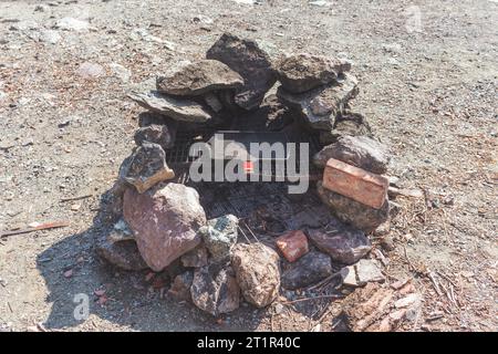 Ein Picknick-Grill aus Ziegeln auf dem Boden und eine eiserne Grillpfanne. Stockfoto