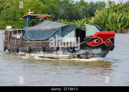 Flussverkehr auf dem Saigon River, in der Nähe von Ho Chi Minh, Vietnam. Black Eyes im White Circle am Prow of Boat sind der traditionelle Schutz gegen Evil River SPI Stockfoto