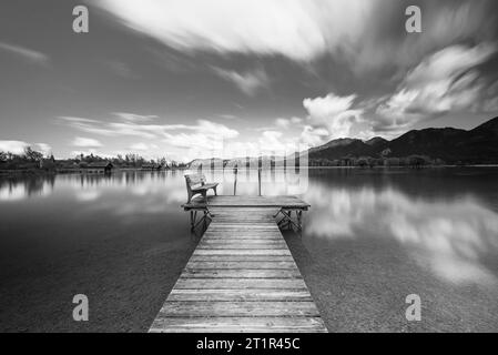 Wolken, die über eine hölzerne Fußgängerbrücke am Ufer des Kochelsees vor herbstlicher Berglandschaft treiben und Wolken am Himmel, Bayern Stockfoto