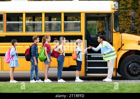 Freundliche Lehrerin, die mit den Kindern im Schulbus herumstolpert Stockfoto