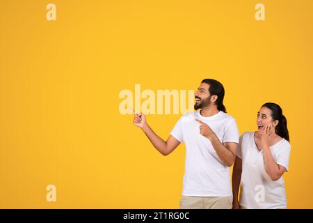 Ein glückliches, schockiertes arabisches Millennial-Paar, das mit den Fingern auf leeren Raum zeigt, für Text oder Werbung Stockfoto