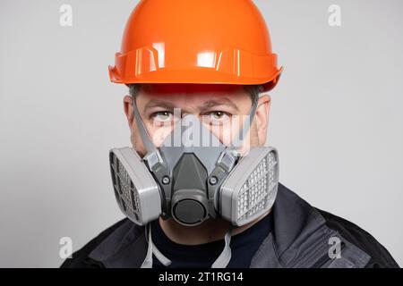 Ein Mann mit Schutzhelm und Atemschutzmaske zum Schutz vor Staub und Gasen auf weißem Hintergrund. Stockfoto