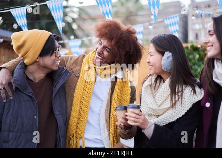 Lachende Freunde trinken zusammen heiße Getränke auf der Straße draußen. Generation z fröhliche Gruppenmenschen. Stockfoto