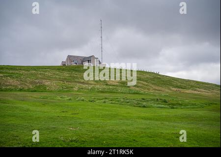 Hausgebäude mit Radarturm auf einem Hügel in der Nähe des Friedhofs auf Shetland Island, Schottland Stockfoto