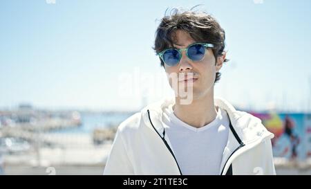 Junger lateinamerikanischer Mann mit ernstem Gesichtsausdruck und Sonnenbrille am Meer Stockfoto