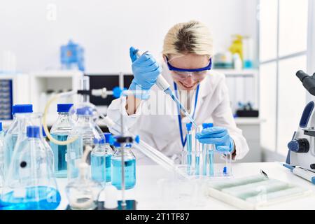 Junge blonde Wissenschaftlerin, die im Labor Flüssigkeit auf das Reagenzglas gießt Stockfoto
