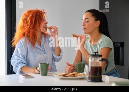 Mutter und Tochter frühstücken zusammen, essen Butterkekse und Kaffee. Familienzeit. Stockfoto