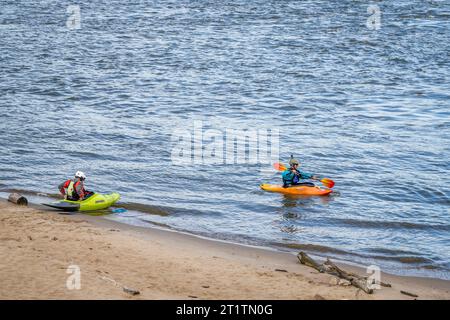 Granite City, Il, USA – 8. Oktober 2023: Zwei Kajakfahrer starten Wildwasserkajaks von einem Strand am Mississippi River unterhalb eines Wassers des Low W Stockfoto