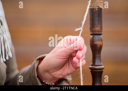 Nahaufnahme von Frauenhänden, die einen Faden auf ein drehendes Rad weben. Die Frau spinnt die Wolle vorsichtig mit einer Tropfenspindel in einen Faden und zeigt ihre SK Stockfoto