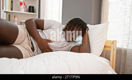 afroamerikaner, der an Magenschmerzen leidet, liegt im Schlafzimmer auf dem Bett Stockfoto