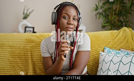 Selbstbewusste afroamerikanische Frau singt ihr Herz aus, chillt zu Hause auf dem Sofa und tanzt zum Beat ihres Lieblingssongs Lost in the Stockfoto