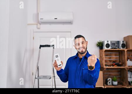 Hispanischer Reparaturmann, der mit der Klimaanlage arbeitet, schreiend stolz, feiert Sieg und Erfolg sehr aufgeregt mit erhobenen Armen Stockfoto