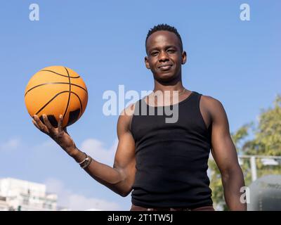 Porträt eines jungen afroamerikanischen Mannes, der auf einem Basketballfeld mit einem Ball in der Hand in die Kamera schaut Stockfoto