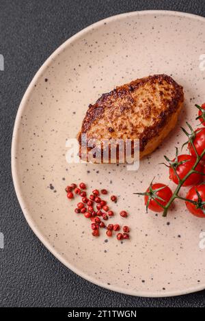 Köstliches frisch gebratenes vegetarisches Sojabohnenschnitzel mit Salz, Gewürzen und Kräutern mit Gemüse auf einer Keramikplatte auf dunklem Betonhintergrund Stockfoto