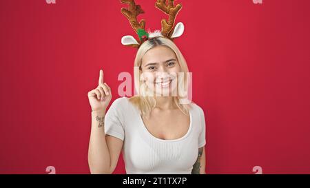 Junge schöne hispanische Frau mit Rentier-weihnachtsmütze mit Ideenausdruck auf isoliertem roten Hintergrund Stockfoto