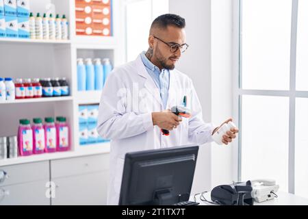 Junger hispanischer Mann Apotheker Scannen Pillen Flasche in der Apotheke Stockfoto