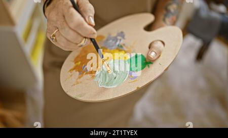 Die Hände einer älteren Künstlerin mischen fröhlich Farben im Kunststudio und beherrschen ihr Hobby Stockfoto