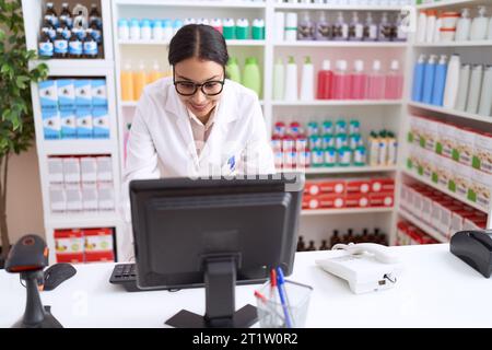 Junge arabische Apothekerin, die selbstbewusst mit dem Computer in der Apotheke lächelt Stockfoto