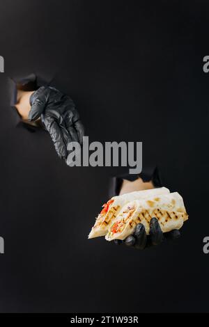 Halten Sie Döner oder Shawarma mit der Hand, und zeigen Sie darauf durch gerissene Löcher im Hintergrund aus schwarzem Papier Stockfoto