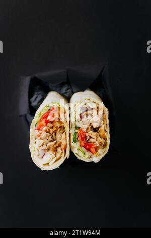 Hände, die Döner oder Shawarma durch gerissene Löcher auf schwarzem Papierhintergrund halten. Street-Food-Konzept Stockfoto