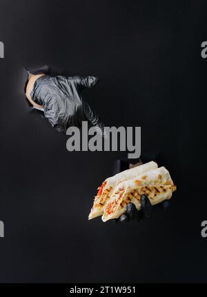 Halten Sie Döner oder Shawarma mit der Hand, und zeigen Sie mit dem Finger durch gerissene Löcher auf schwarzem Papierhintergrund darauf Stockfoto
