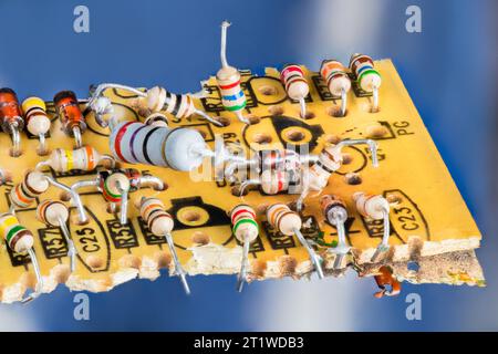 Entsorgung von Elektroschrott verschiedener elektrischer Komponenten auf alten gebrochenen gelben Leiterplatten mit blauem Hintergrund. Nahaufnahme von farbkodierten Widerständen und Siliziumdioden. Stockfoto