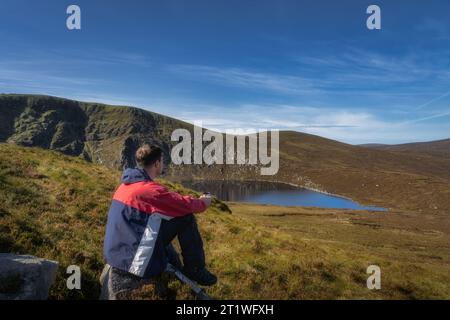 Männer, die auf einem Felsen sitzen und Kaffee oder Tee aus der Thermoskanne trinken. Panoramablick auf Lough Ouler und Tonelagee Mountain, Wandern in den Wicklow Mountains, Irland Stockfoto