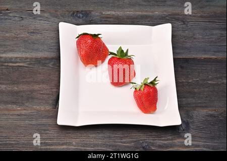 Erdbeeren auf einem weißen quadratischen Teller auf hölzernem Hintergrund. Konzept Stockfoto