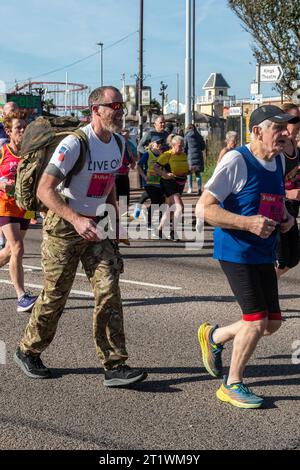 Great South Run, 15. Oktober 2023, Portsmouth, Hampshire, England, UK. Tausende von Teilnehmern liefen im 16-Mile-Great South Run in Southsea, Portsmouth. Neben den Elite-Läufern nahmen auch viele andere Teilnehmer Teil, die für Wohltätigkeitsorganisationen oder ihre Vereine gelaufen waren. Im Bild: Soldat, der mit einem schweren Rucksack läuft und Geld für die Royal British Legion-Wohltätigkeitsorganisation sammelt Stockfoto