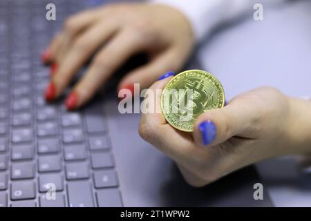 Bitcoin in den Händen eines Mädchens, das am Laptop arbeitet, elektronisches dezentralisiertes Geld, Kryptowährung Stockfoto