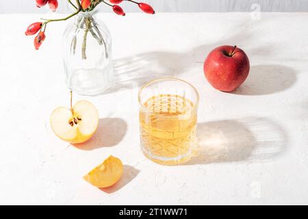 Frische reife Äpfel und ein Glas Apfelsaft oder Cidre auf weißem Tisch im Sonnenlicht. Herbsternte, Thanksgiving-Konzept. Draufsicht. Stockfoto