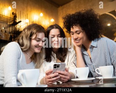 Eine Gruppe verschiedener weiblicher Freunde, die in einem Café auf Smatphone stöbern Stockfoto