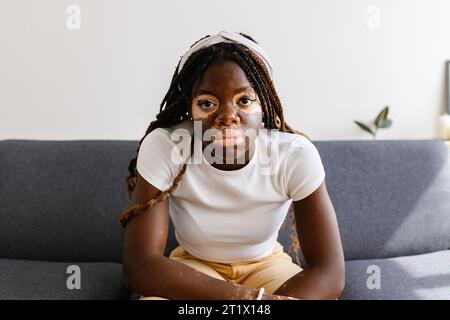 Ernsthaftes Porträt einer jungen afrikanerin mit Vitiligo, die auf Sofa sitzt Stockfoto