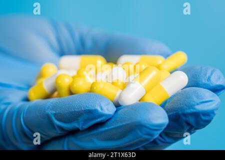 Arzt, Apotheker oder Wissenschaftler Hand in Handschuhen mit Pillen, Vitaminen oder Nahrungsergänzungsmitteln auf blauem Hintergrund. Medizin oder medikamentöse Therapie, wissenschaftliche Forschung Stockfoto
