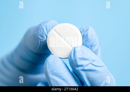 Weiße Brause- oder Kohletablette in der Hand im Entsorgungshandschuh. Arzt, Apotheker oder Wissenschaftler Finger halten Pille, Vitamin oder Nahrungsergänzungsmittel auf Blau Stockfoto