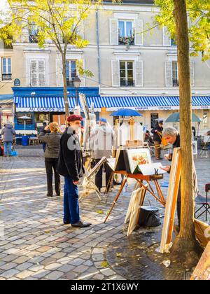 Ein lächelnder französischer Künstler trägt eine rote Baskenmütze und zeigt Bilder zum Verkauf am Place du Tertre, Montmartre, 18. Arrondissement, Paris, Frankreich Stockfoto