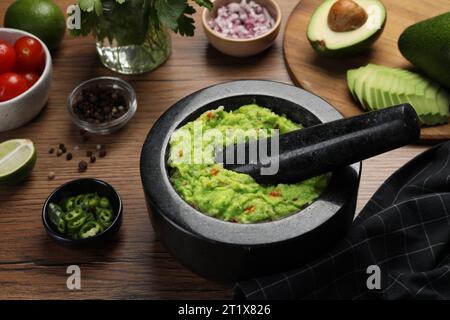 Köstliche Guacamole in Mörtel und Zutaten auf Holztisch, Nahaufnahme Stockfoto