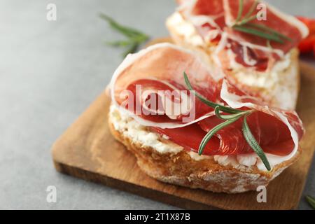 Leckere Sandwiches mit Räucherschinken und Rosmarin auf grauem Tisch, Nahaufnahme Stockfoto