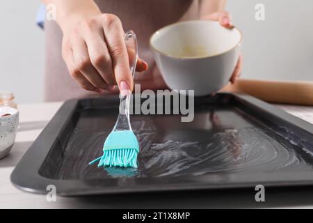 Ich mache köstliche Baklava. Eine Frau, die Backpfanne am weißen Tisch buttert, Nahaufnahme Stockfoto