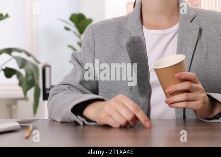 Frau zeigt Flecken von Kaffee auf ihrer Jacke an Holztisch drinnen, Nahaufnahme Stockfoto