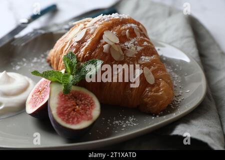 Leckeres Croissant mit Feigen, Mandelflocken und Sahne auf dem Tisch, Nahaufnahme Stockfoto