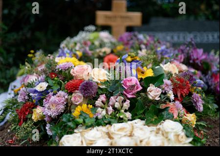 Trauerkranz auf einem Grab mit bunten Blumen und einem Holzkreuz in einem verschwommenen Hintergrund Stockfoto