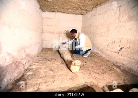 Minya, Ägypten. Oktober 2023. Ein Archäologe reinigt eine Mumie in einem Grabmal auf einem Friedhof in Minya Governorate, Ägypten, 15. Oktober 2023. Ein Friedhof aus dem Neuen Königreich des alten Ägypten wurde in der Nekropole Thuna El-Gebel im südägyptischen Gouvernement Minya entdeckt, wie das ägyptische Ministerium für Tourismus und Antiquitäten am Sonntag bekannt gab. Quelle: Ahmed Gomaa/Xinhua/Alamy Live News Stockfoto