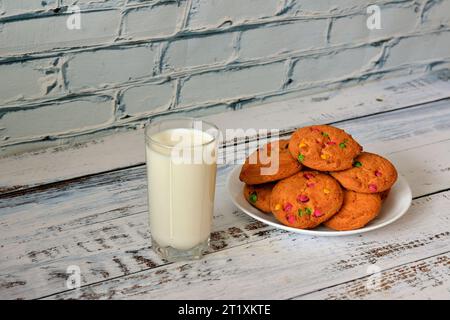 Ein Teller mit einem Haufen Haferflocken in mehrfarbiger Glasur und einem Glas heißer Milch auf einem hellen Holztisch. Nahaufnahme. Stockfoto
