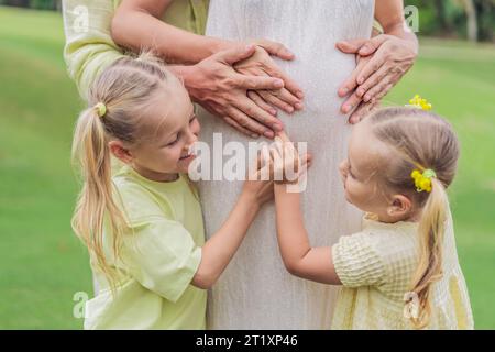 Die Liebe der Schwestern blüht, während sie den schwangeren Bauch ihrer Mutter zärtlich umarmen und ihre Vorfreude und Zuneigung für ihre bald ankommenden Geschwister teilen Stockfoto