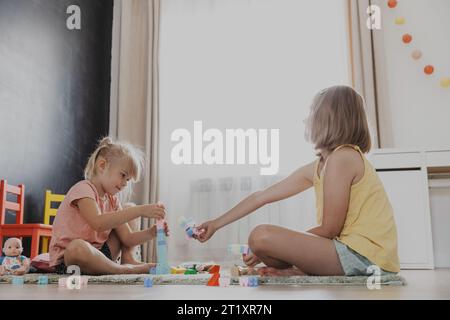 Kinder spielen mit bunten Bausteinen, Ziegeln. Kinder sitzen auf dem Boden drinnen im sonnigen weißen Schlafzimmer oder Kindergarten, Spielzentrum. Lustiges pädagogisches, umweltfreundliches Spiel für Kinder Stockfoto